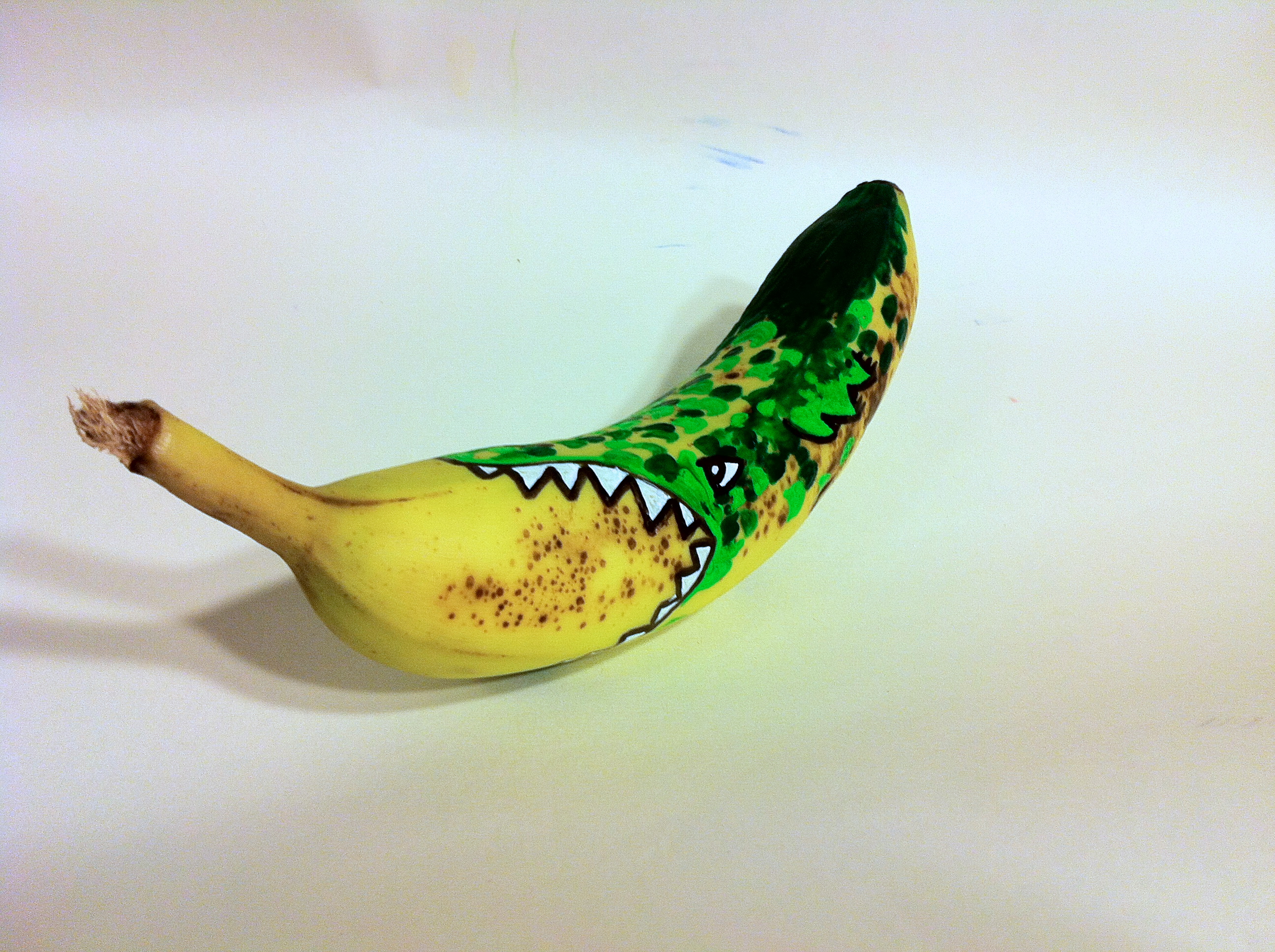 Painted banana, a green monster is painted on to the banana. this creates an illusion that the monster is eating the banana.